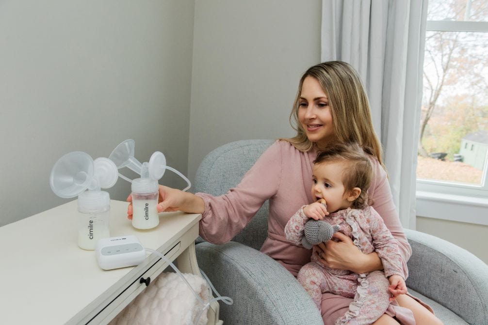 Cimilre-E1-breast-pump-after-pumping Cimlre E1 Breast Pumping Bottles With Mother Siting On Chair Holding Baby